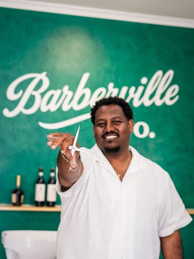 Thomas, owner of Barberville Co., holding barber scissors inside the West Richmond barbershop